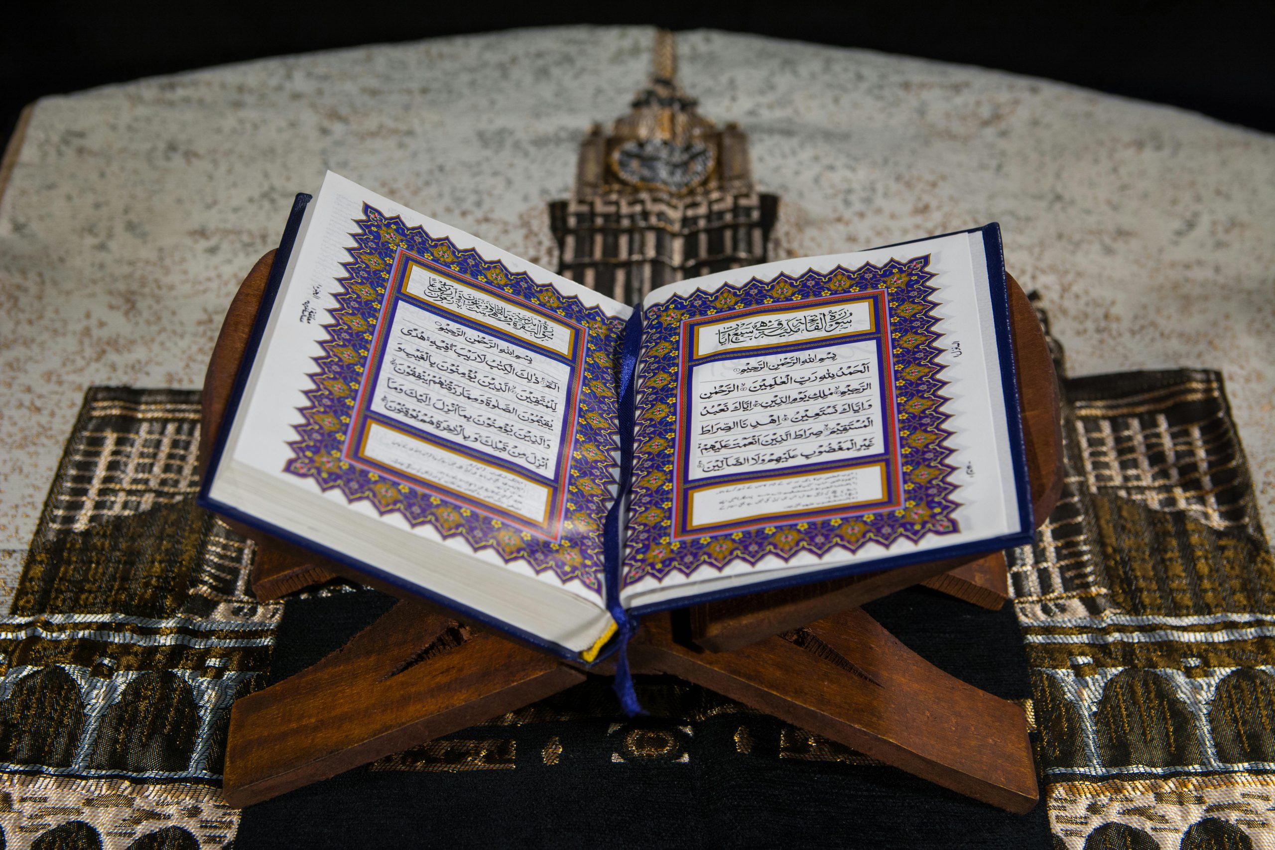 An open Quran on a wooden stand atop a prayer rug, emphasizing Islamic faith.